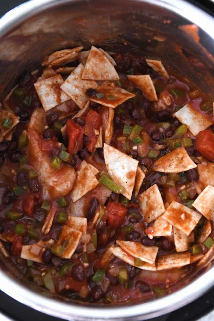 Top down view of an InstantPot filled with raw chicken, black beans, crushed tomatoes, green chiles, and cut up tortillas.