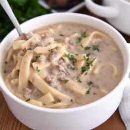 Spoon in bowl with beef stroganoff soup topped with fresh parsley.
