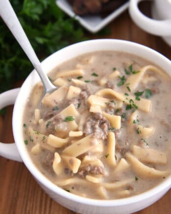 Spoon scooping up bite of thick noodles, broth and ground beef.