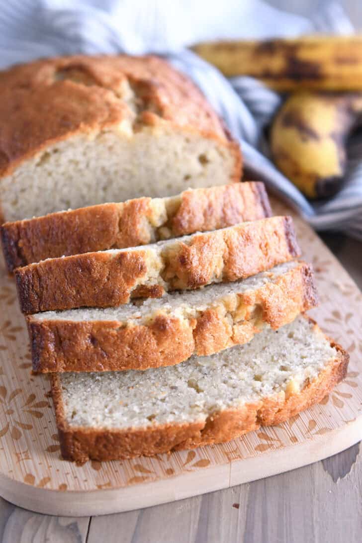 Four slices of buttermilk banana bread on wood cutting board.