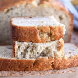 Two half slices of banana bread on wood cutting board.