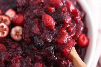 Wooden spoon scooping bite of cranberry chutney in white bowl.