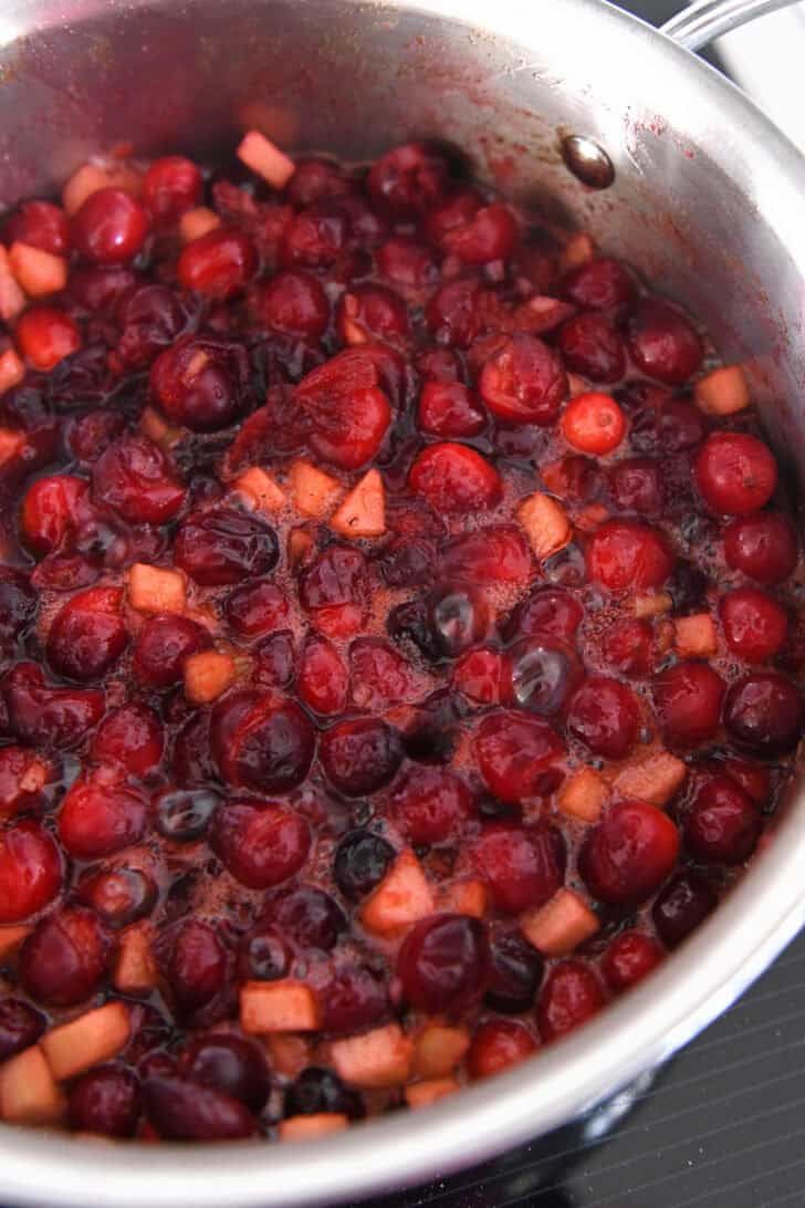 Simmering mixture of green apples, cranberries, sugar, and cinnamon.