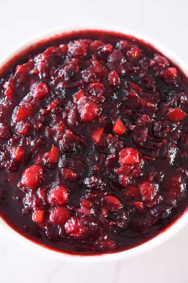 Top down view of thick cranberry chutney in white bowl.