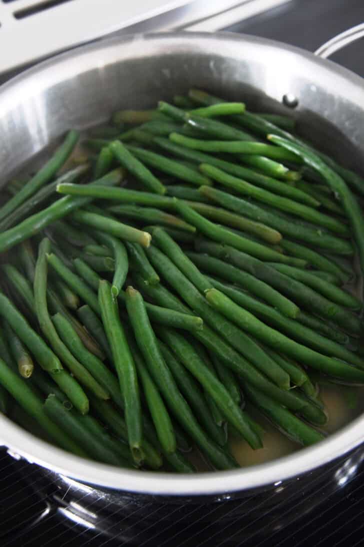 Cooked green beans in chicken broth in skillet.