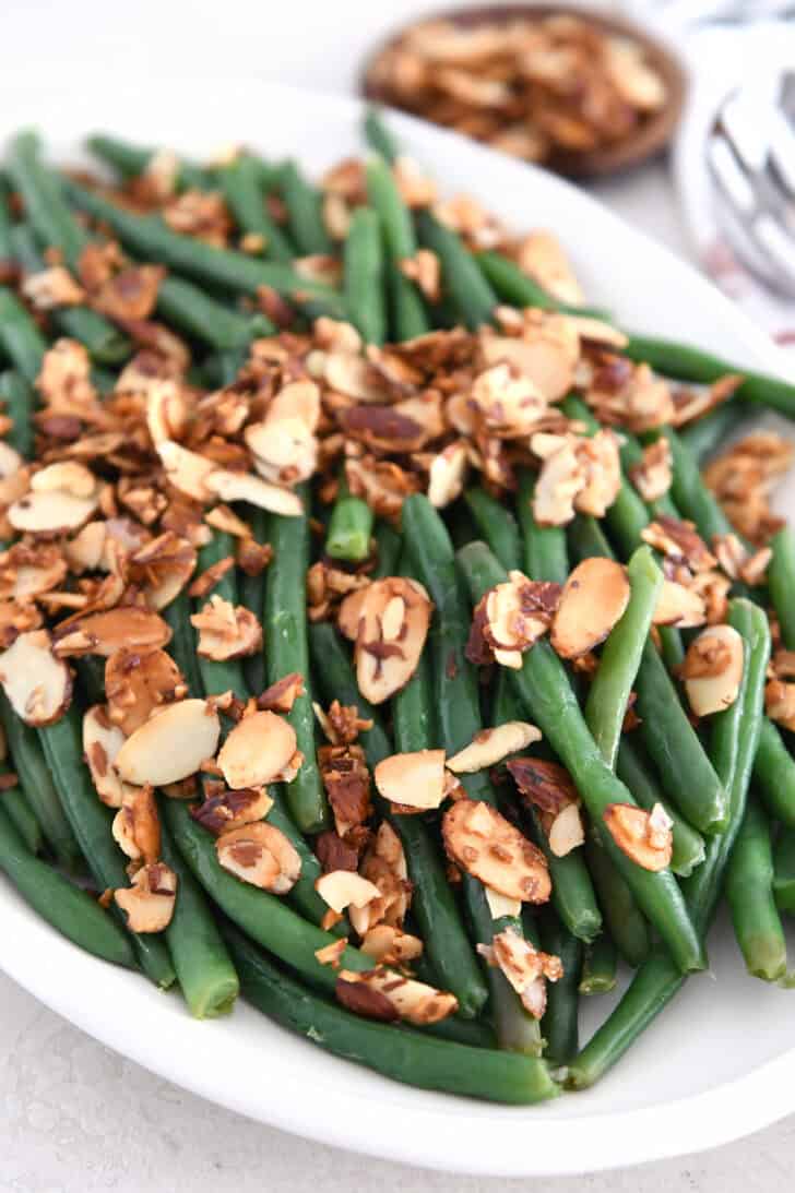 White tray with steamed green beans, toasted almonds, and garlic.