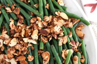Top down view of sauteed green beans on white tray with toasted almonds.
