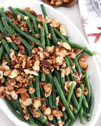 Top down view of sauteed green beans on white tray with toasted almonds.