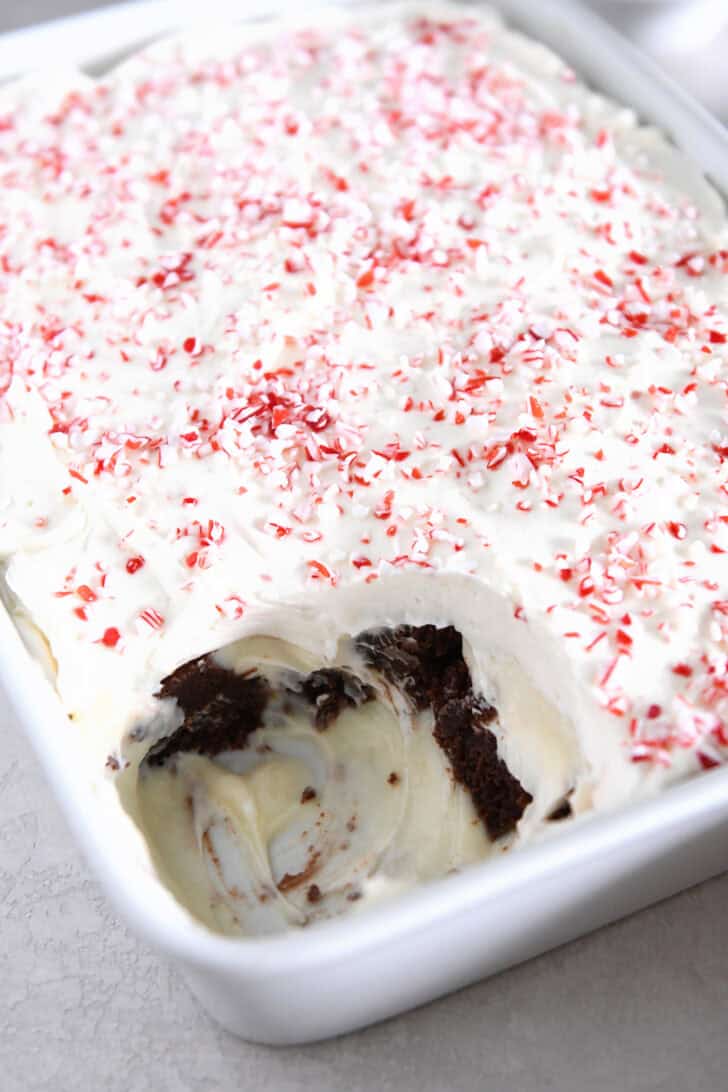 Scoop taken out of brownie peppermint bark pudding trifle in white dish.