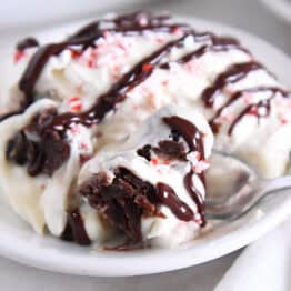 Spoon scooping bite of brownie pudding trifle on white plate.