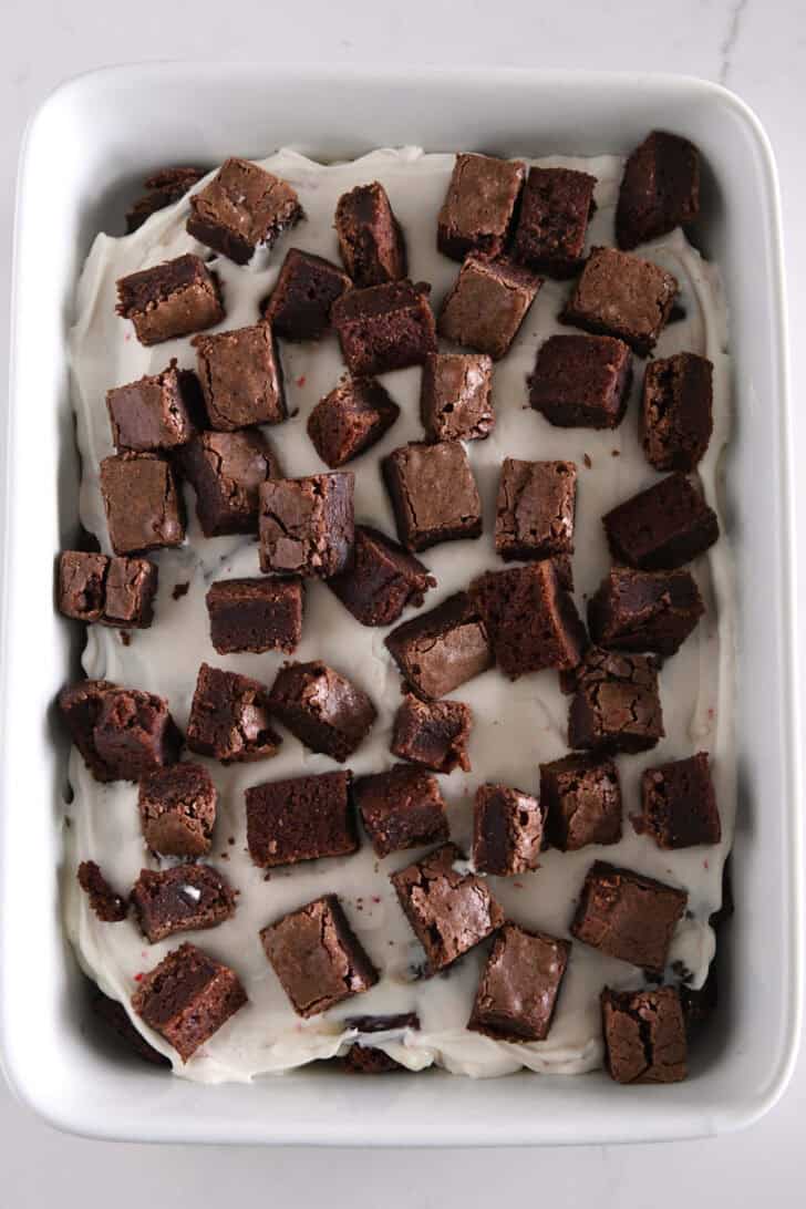 Brownie cubes on top of peppermint cream cheese layer in white dish.