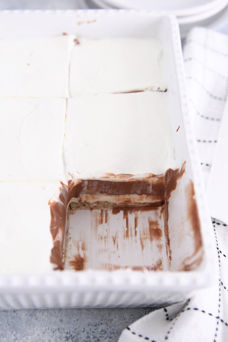 White 9X13-inch pan with layered dessert of shortbread crust, chocolate pudding, no-bake cheesecake and whipped cream with one square removed.