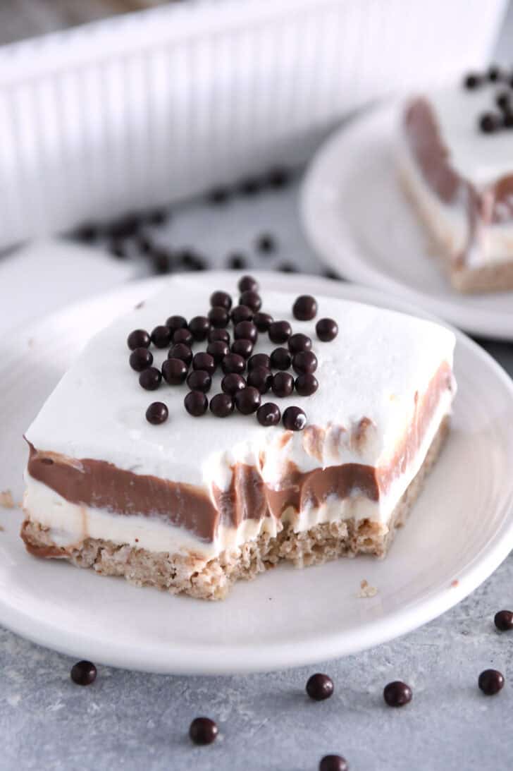 Bite taken out of square of chocolate pudding delight dessert on white plate.