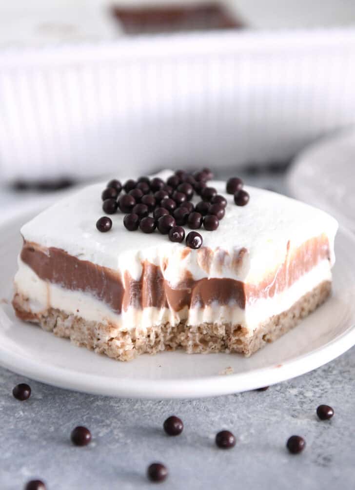 Bite taken out of square of chocolate pudding delight dessert on white plate.