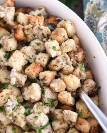 Spoon nestled under baked stuffing in white dish.