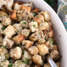 Spoon nestled under baked stuffing in white dish.