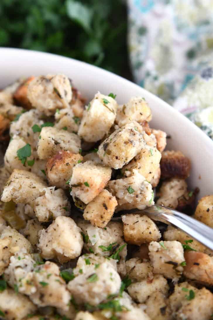 Spoon scooping up stuffing in white dish.