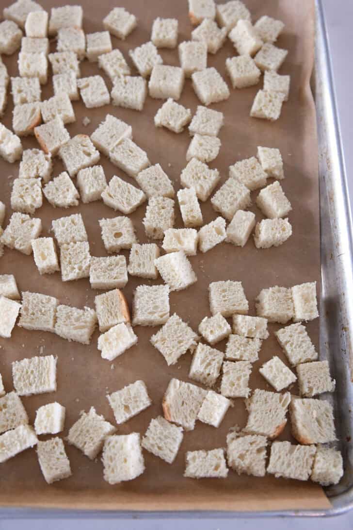 Bread cubes on parchment-lined baking sheet.