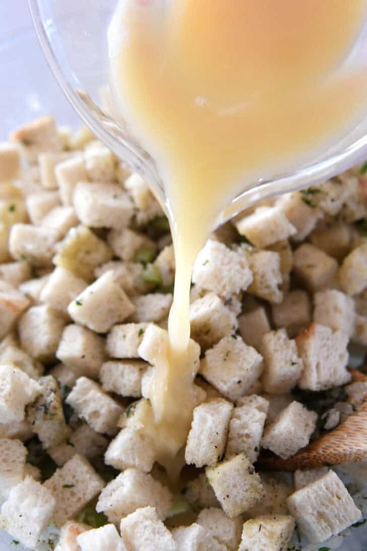 Pouring broth and eggs into toasted bread cubes.