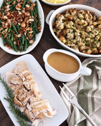Top down view of platters of slow cooker turkey breast, gravy, stuffing, green beans and mashed potatoes.