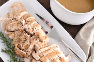 White platter with cooked turkey, rosemary, gravy boat, stuffing and green beans.