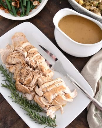 White platter with cooked turkey, rosemary, gravy boat, stuffing and green beans.