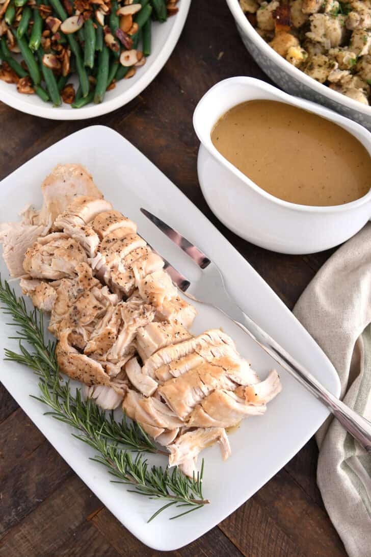 White platter with cooked turkey, rosemary, gravy boat, stuffing and green beans.