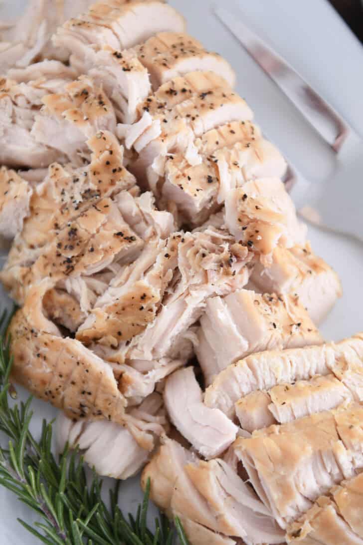 Top down view of cooked turkey breast slices on white platter.