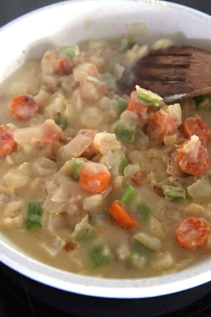 White skillet with thick sauce, carrots, celery and onions.