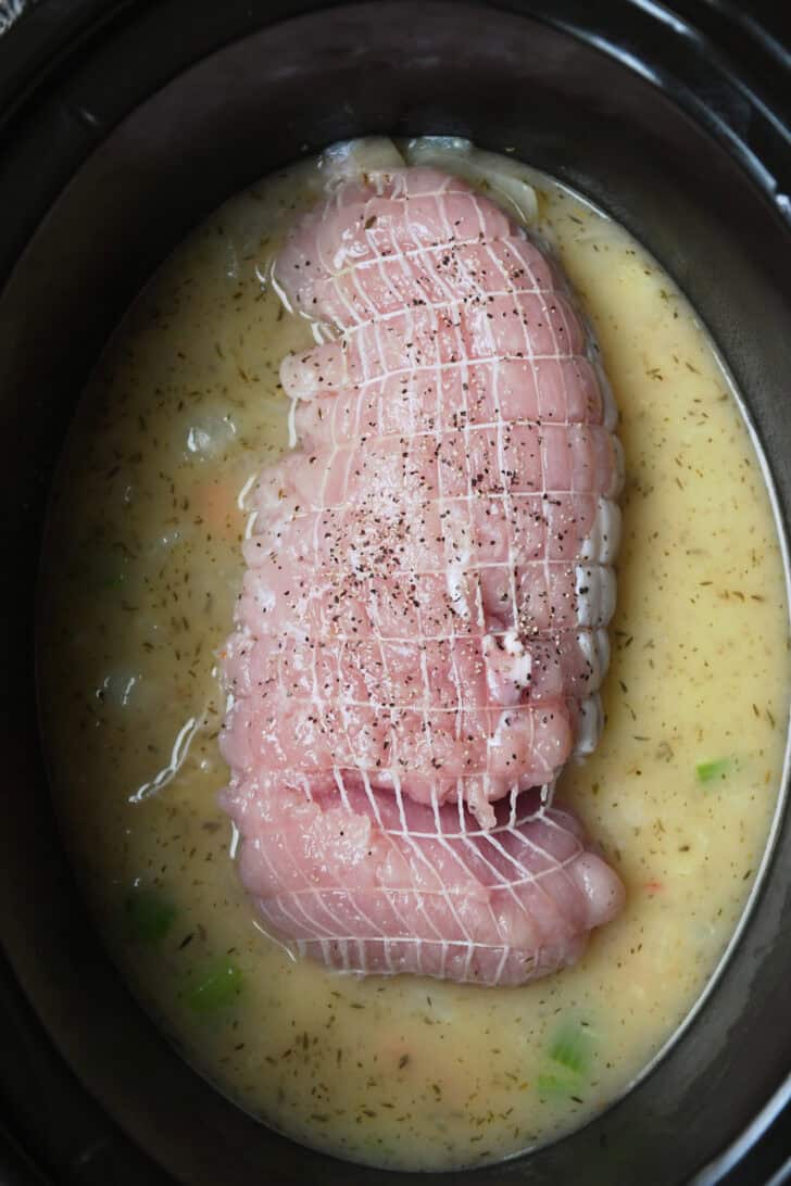 Top down view of turkey breast in slow cooker with broth and veggies.
