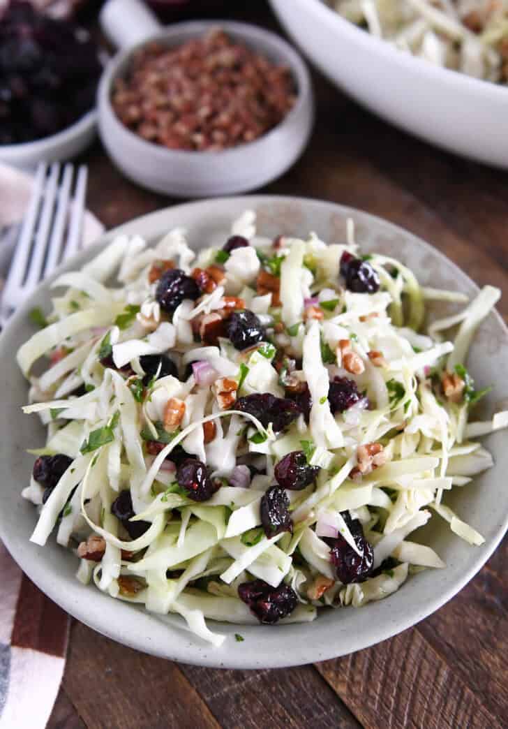 Gray bowl with Thanksgiving slaw with dried cranberries, pecans and red onions.