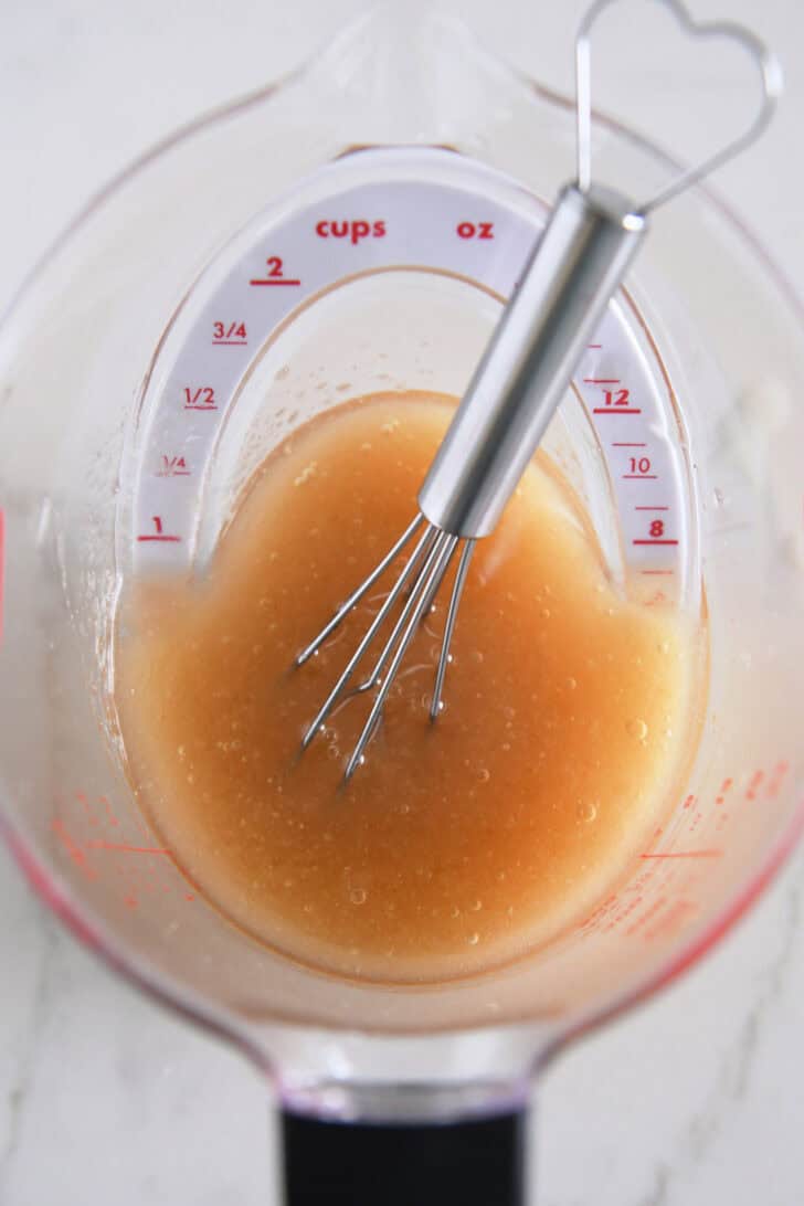 Small whisk in liquid measuring cup with vinaigrette.