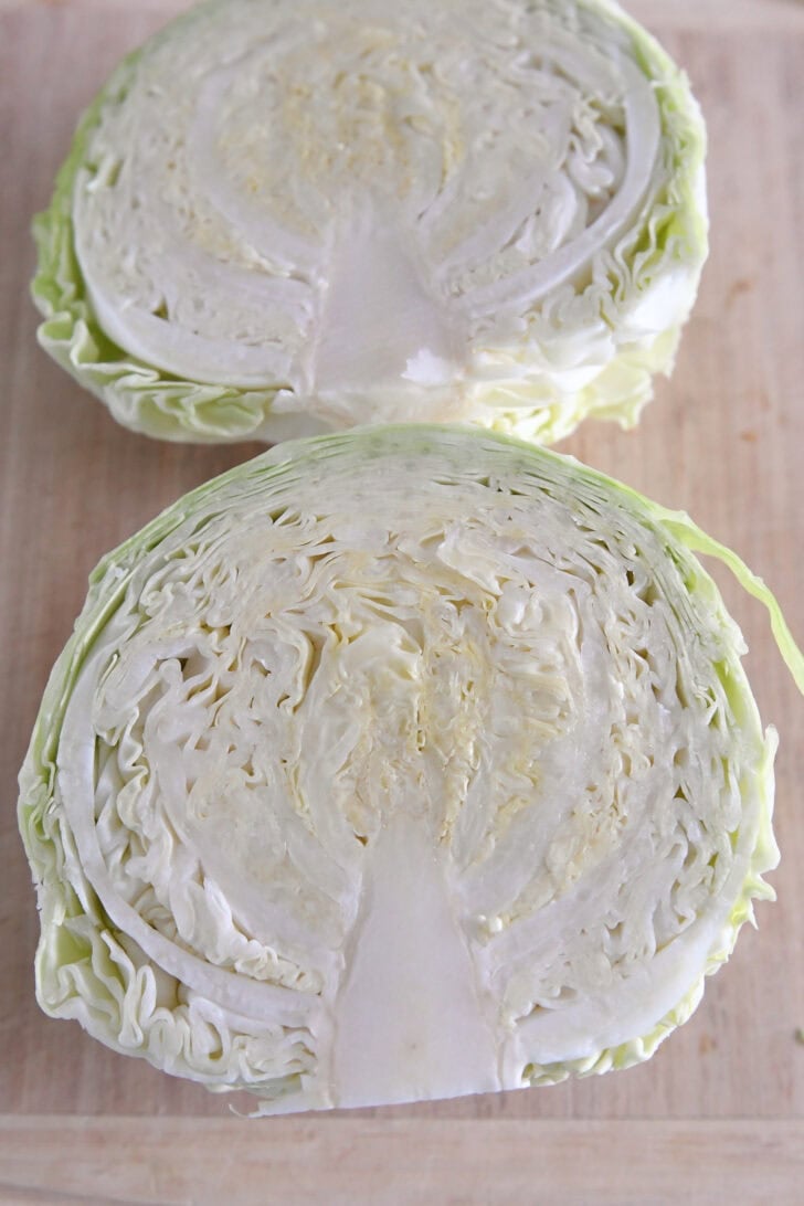 Two half green cabbages on wood cutting board.
