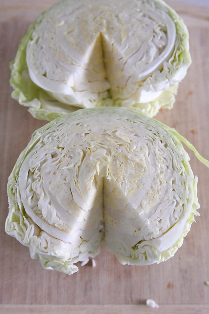 Two half green cabbages on wood cutting board with core removed.