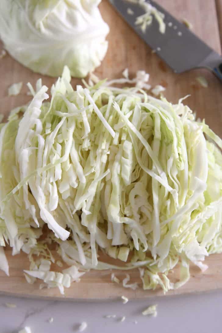 Thin slices of green cabbage on wood cutting board.