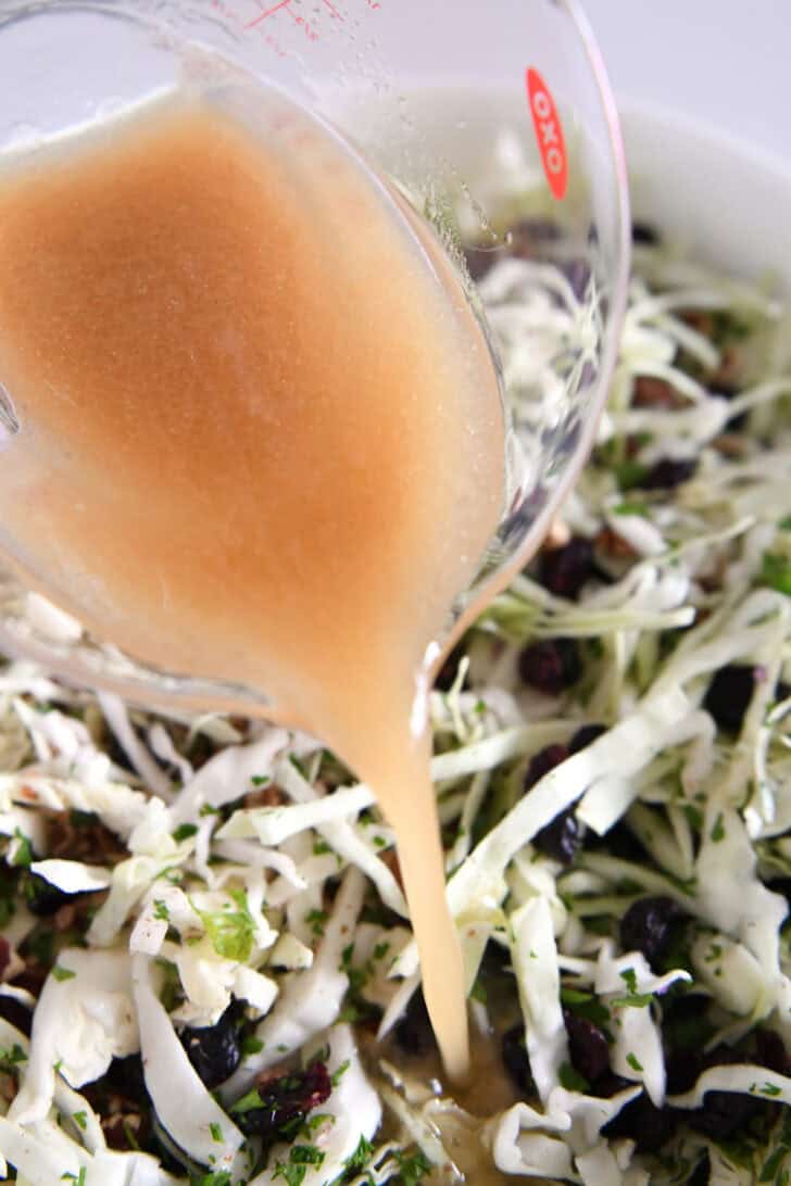 Pouring vinaigrette from liquid measuring cup onto thinly sliced cabbage salad.