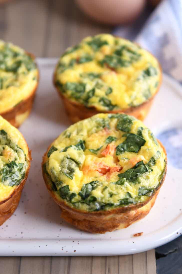 A white platter with golden brown cooked egg and vegetable muffins.