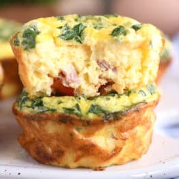 Two cooked egg and veggie muffins cups stacked on top of each other with a bite taken out of the top egg muffin.