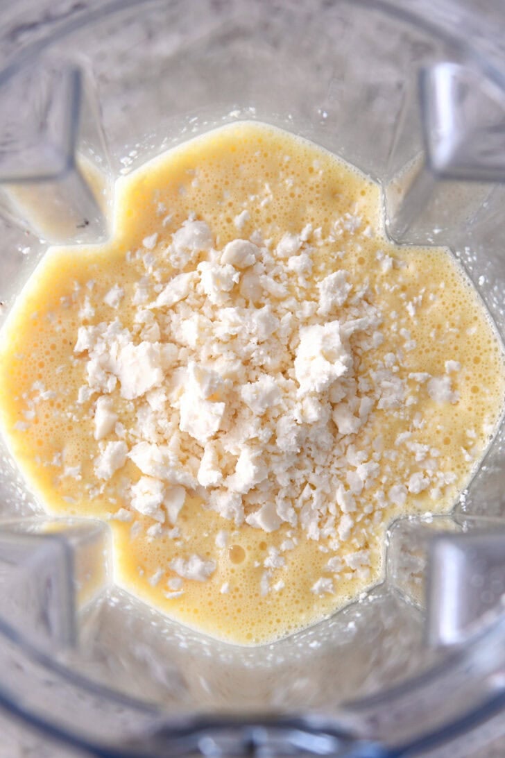 Top down view of a blender full of raw blended eggs and feta cheese.