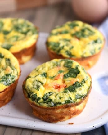 A white platter with golden brown cooked egg and vegetable muffins.