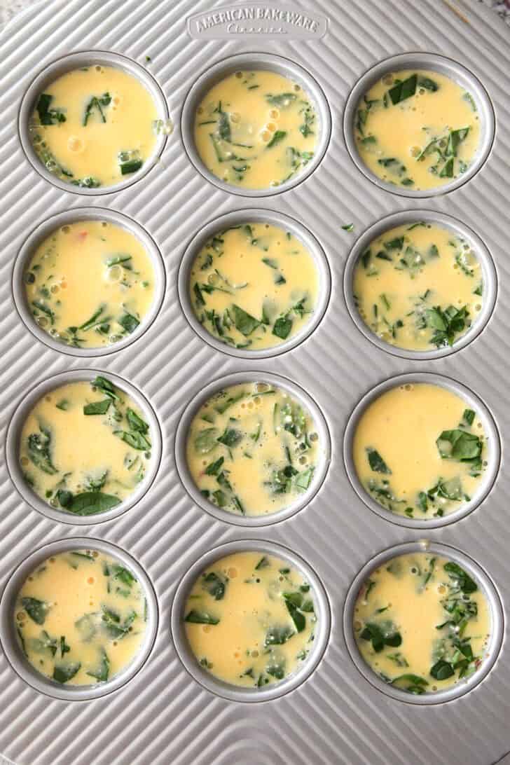 Top down view of uncooked egg and chopped veggies in a muffin tin.