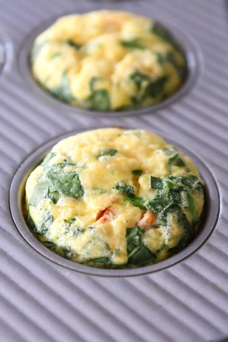 Two cooked egg and veggie muffin cups in a muffin tin.