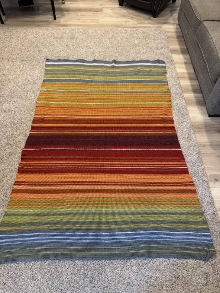 Crocheted temperature blanket laid out on carpet.