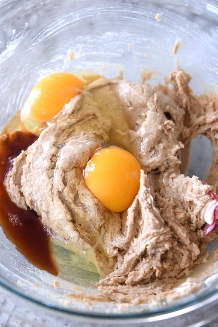 Top down view of a glass bowl with batter, raw eggs, and vanilla extract.