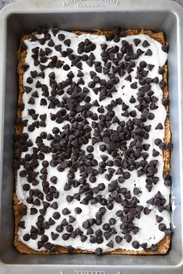 Top down view of a metal pan with chocolate chips sprinkled all over a layer of gooey marshmallow.