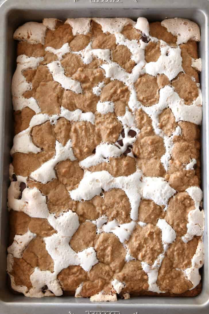 Top down view of a slap of baked s'mores cookie bars with fissures of gooey marshmallow and chocolate chips throughout the golden brown bars.