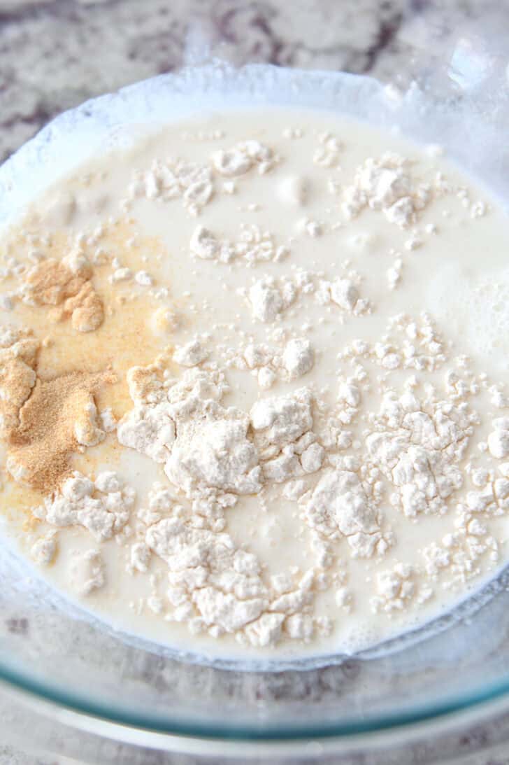 Top down view of a glass bowl with milk, flour, and seasonings.