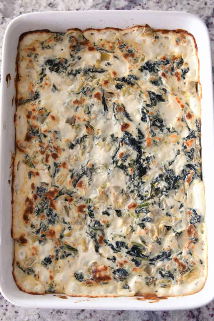 Top down view of a white casserole dish full of golden brown, cooked, creamy spinach artichoke dip.