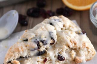 Single cranberry orange scone drizzled with glaze on sheet of parchment paper.