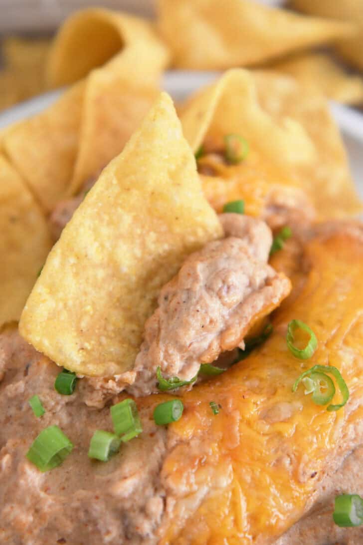 Tortilla chip scooping bite of warm bean dip with cheese and green onions.